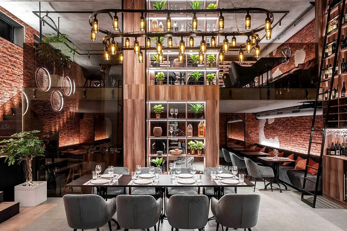 The Divus dining room: a long table under the bulb chandelier, two floors of wine shelves